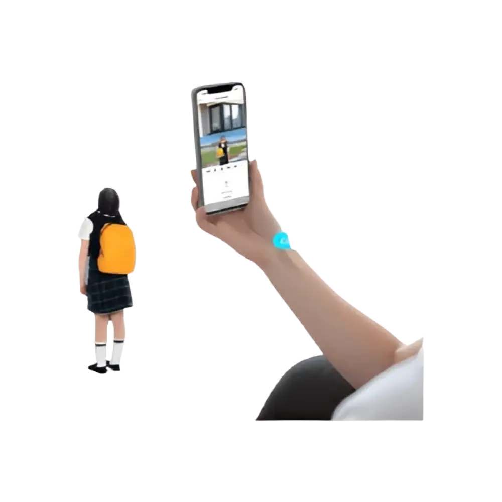 Un enfant portant un sac à dos jaune et une jupe sombre se tient à côté d’un adulte tenant un smartphone levé avec un bracelet de poignet bleu.